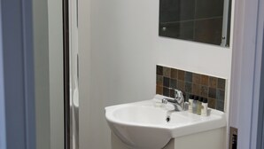 A bathroom with a glass shower enclosure, a sink with a mirror above it, and a toilet. - Hotel Rafay (Blackburn)