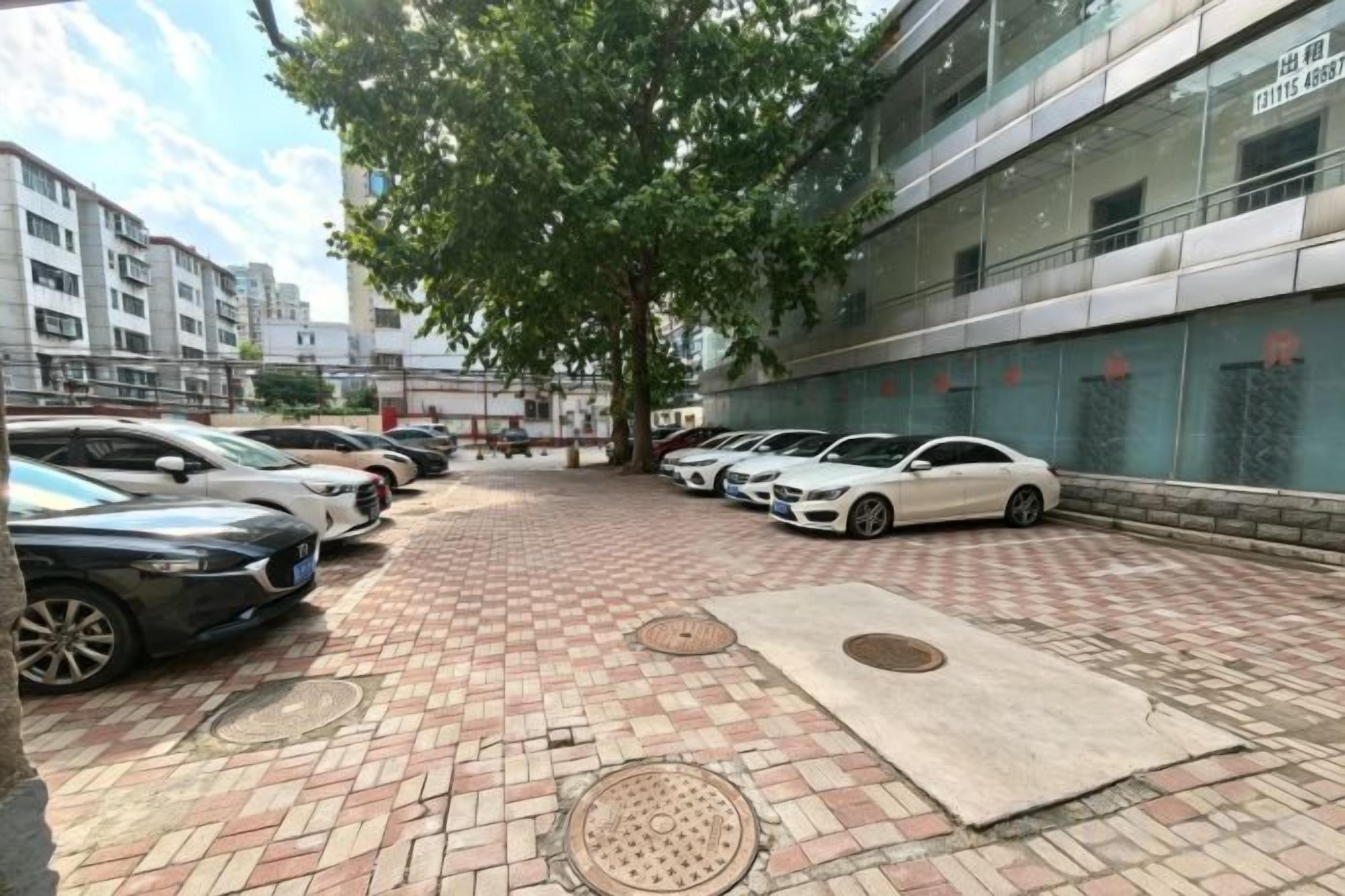 A parking area with cars, a brick pathway, and a building with large windows.