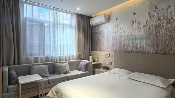 A modern hotel room with a large bed, a sofa, a small table, and a wall-mounted air conditioner. - Yijia 365 Chain Hotel (Shijiazhuang Canal Bridge Railway University Yitang Metro Station Branch) (Shijiazhuang)