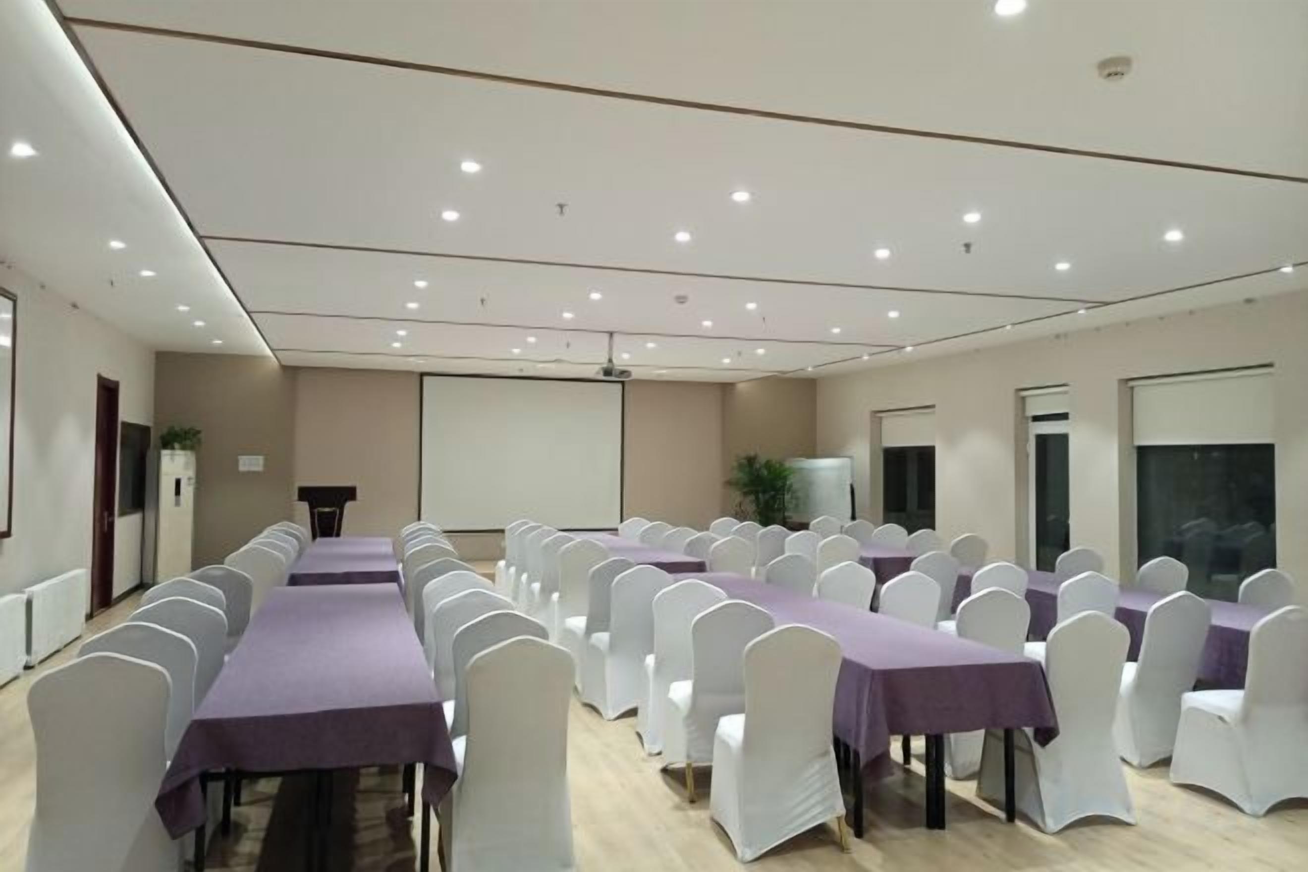 A conference room with rows of tables and chairs, a projector screen, and a podium.