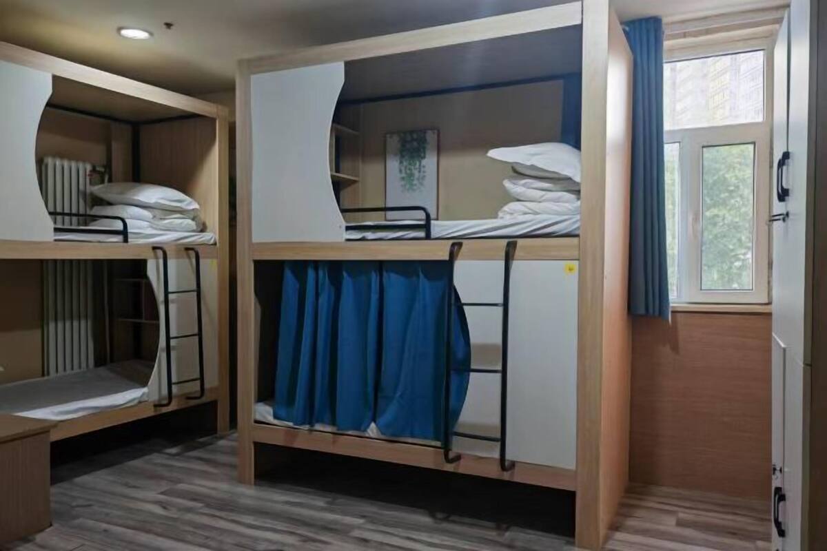 Ein Schlafsaalzimmer mit Etagenbetten, einem kleinen Schreibtisch und einem Fenster mit Vorhängen.