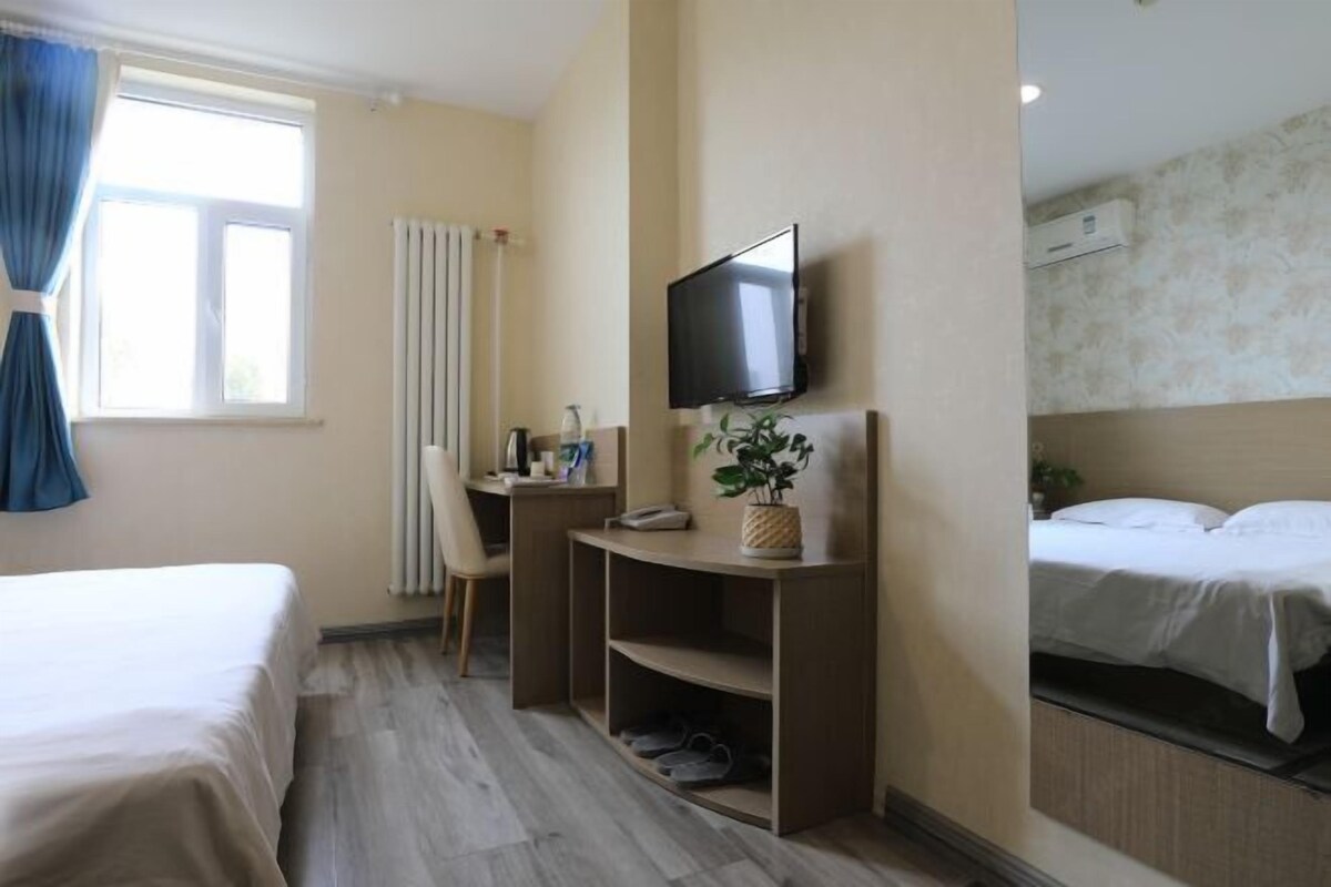 Ein Hotelzimmer mit Bett, Schreibtisch mit Fernseher, Stuhl, kleiner Ablagefläche und einem fenster mit Vorhängen.