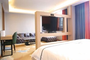 Ein Hotelzimmer mit einem Bett, einem Schreibtisch mit Stuhl, einer Couch und einem Fernseher.
