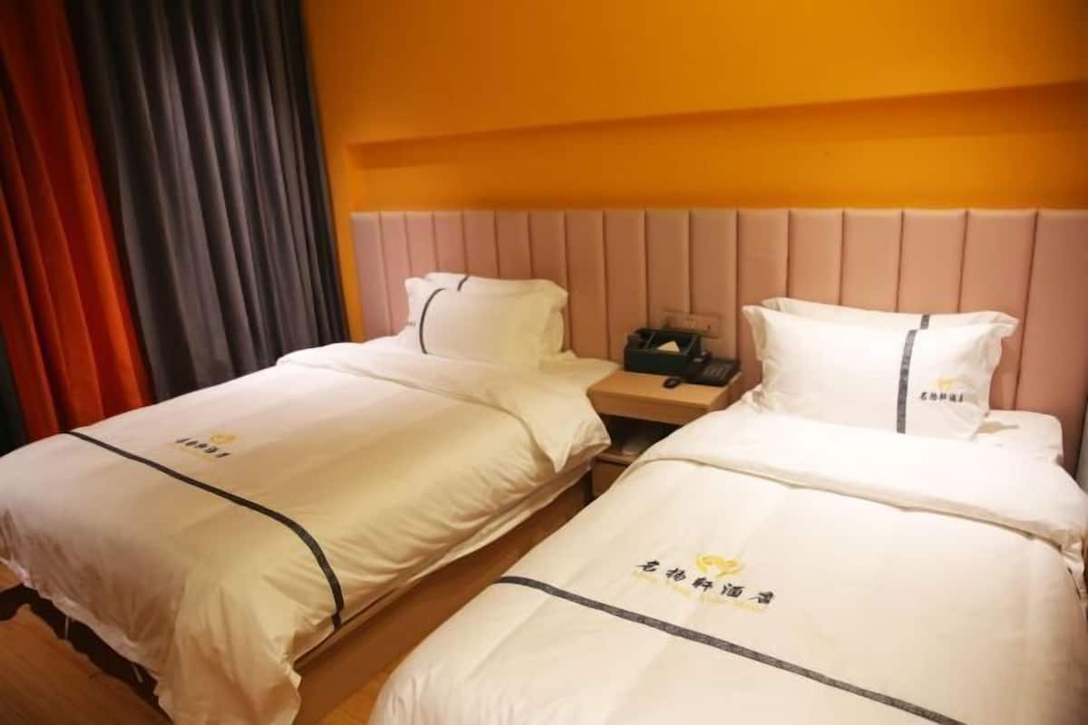 Ein Hotelzimmer mit zwei Betten, jeweils mit Kopfkissen und Decke, einem Nachttisch aus Holz und einer Wand mit einer horizontalen Leuchte.