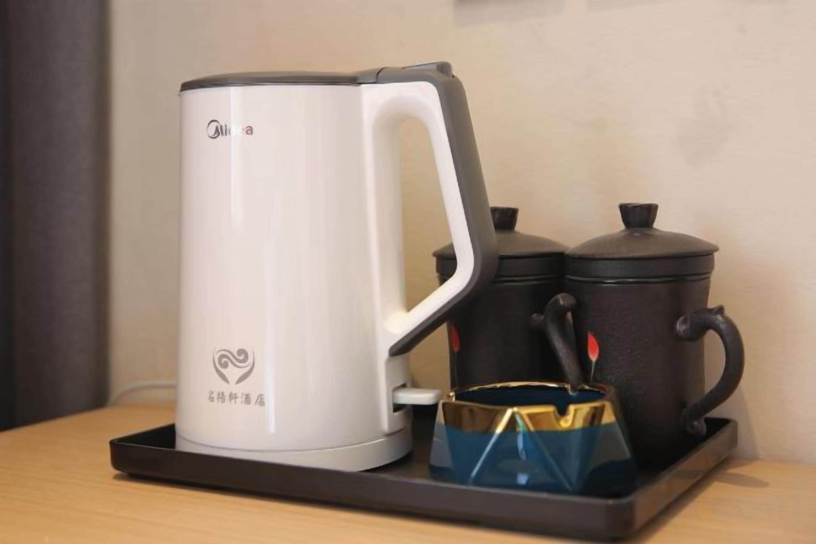 A white electric kettle, a black pot, and a blue mug on a tray.