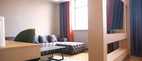 A modern hotel room with a sofa, a small table, a window with curtains, and a bunk bed.