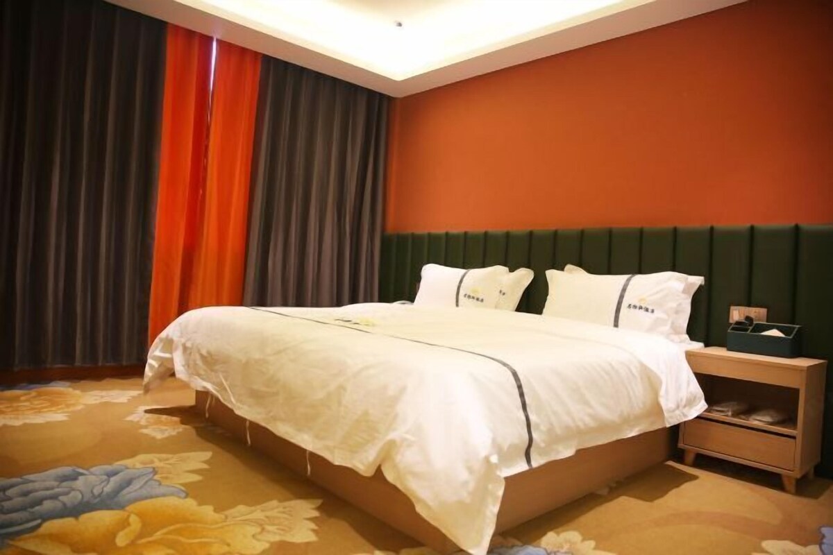 A hotel room with a bed, a nightstand, and a window with curtains.