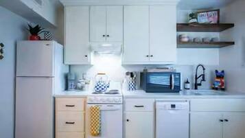 A kitchen with white cabinets, a microwave, a kettle, and a sink.