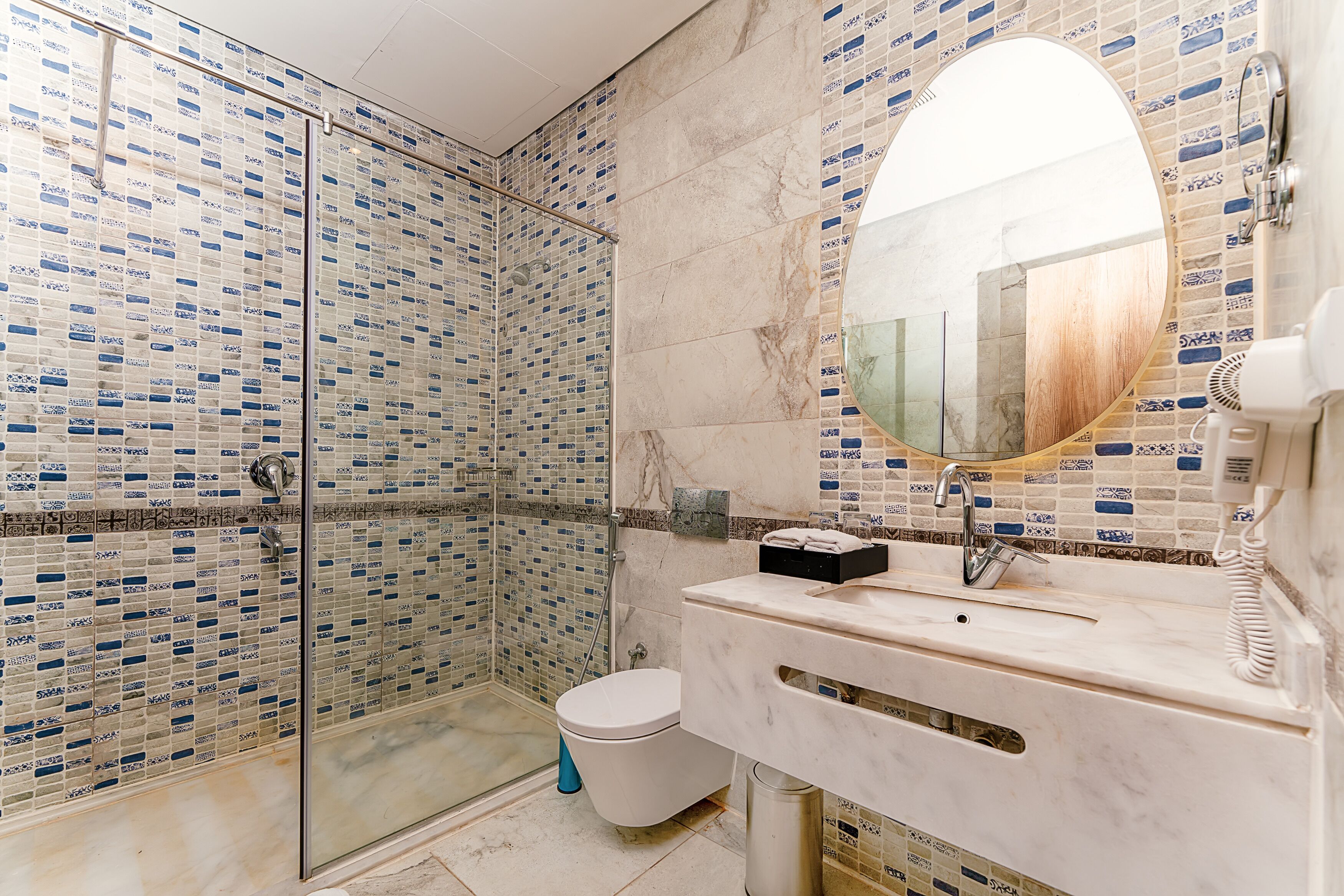 A bathroom with a glass-enclosed shower, a toilet, a sink with a mirror, and a towel rack.