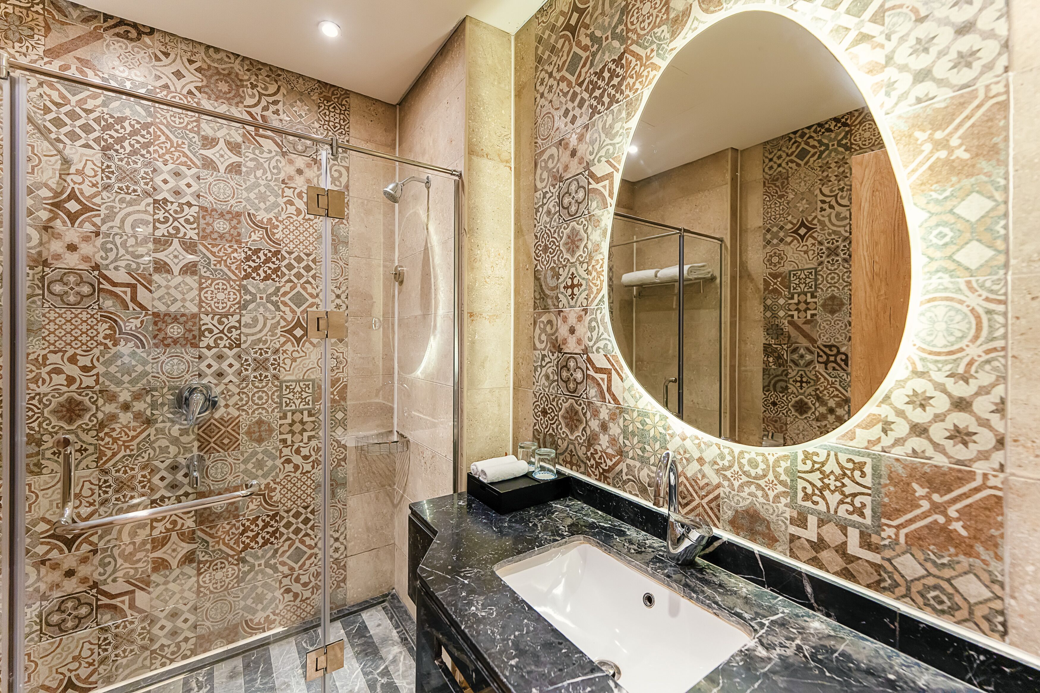 A bathroom with patterned tiles, a glass shower enclosure, a sink with a marble countertop, and a large mirror.