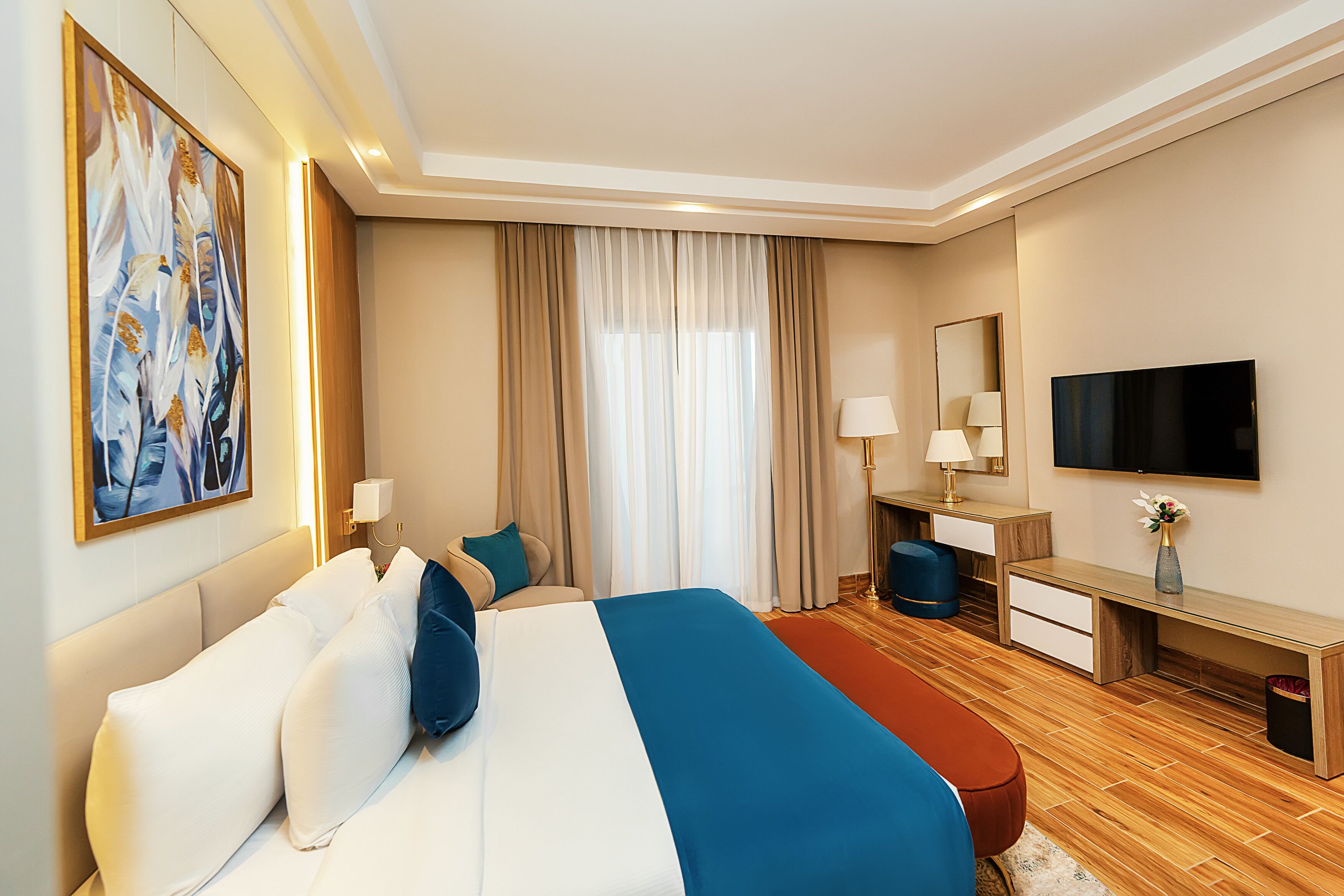 A hotel room with a bed, a desk, a TV, and a large painting on the wall.