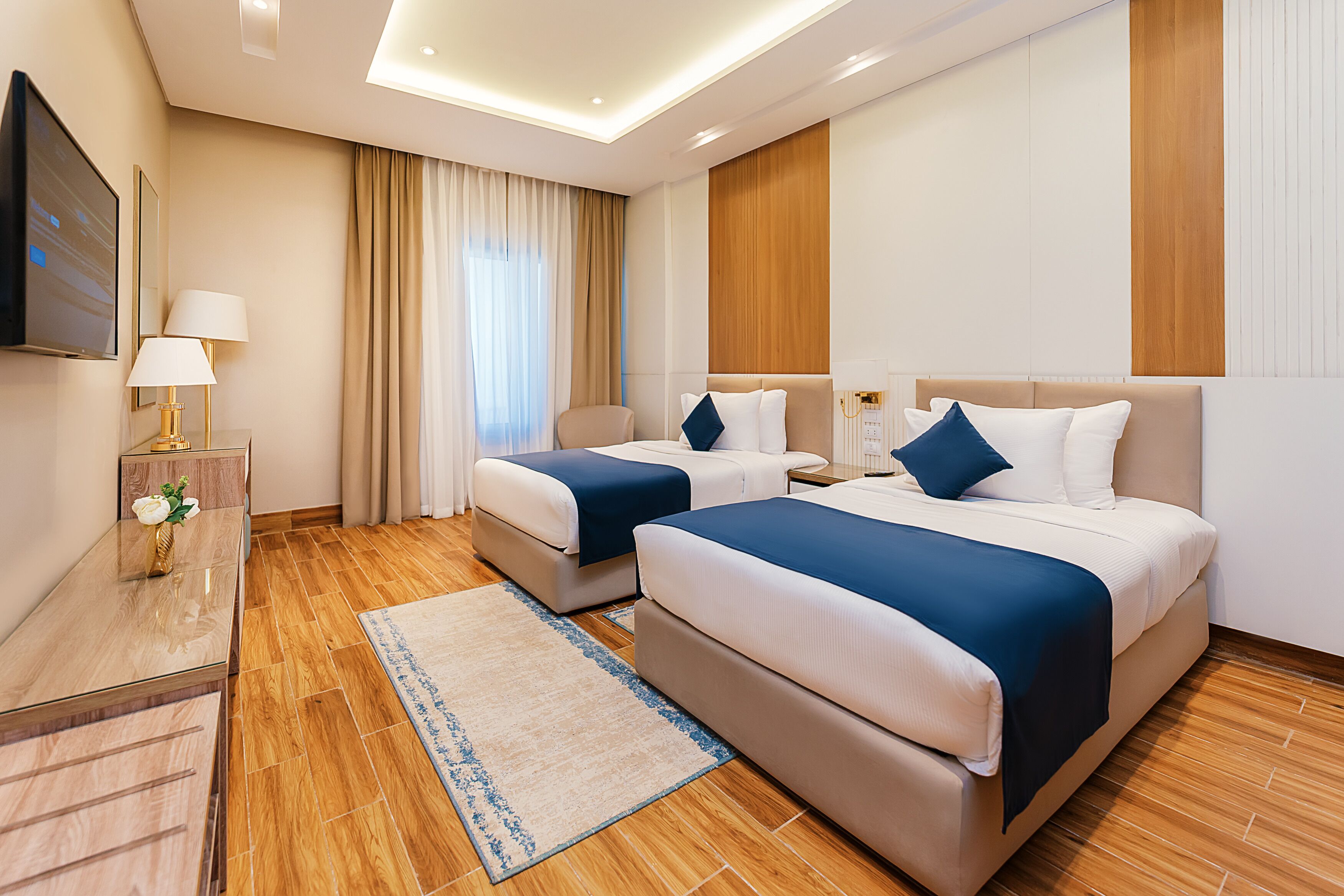 Habitació d'hotel amb dos llits, un televisor, escriptori amb làmpada i terra de fusta.