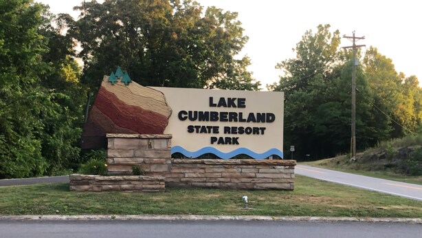 A sign for Lake Cumberland State Resort Park with a stone base and a painted landscape.