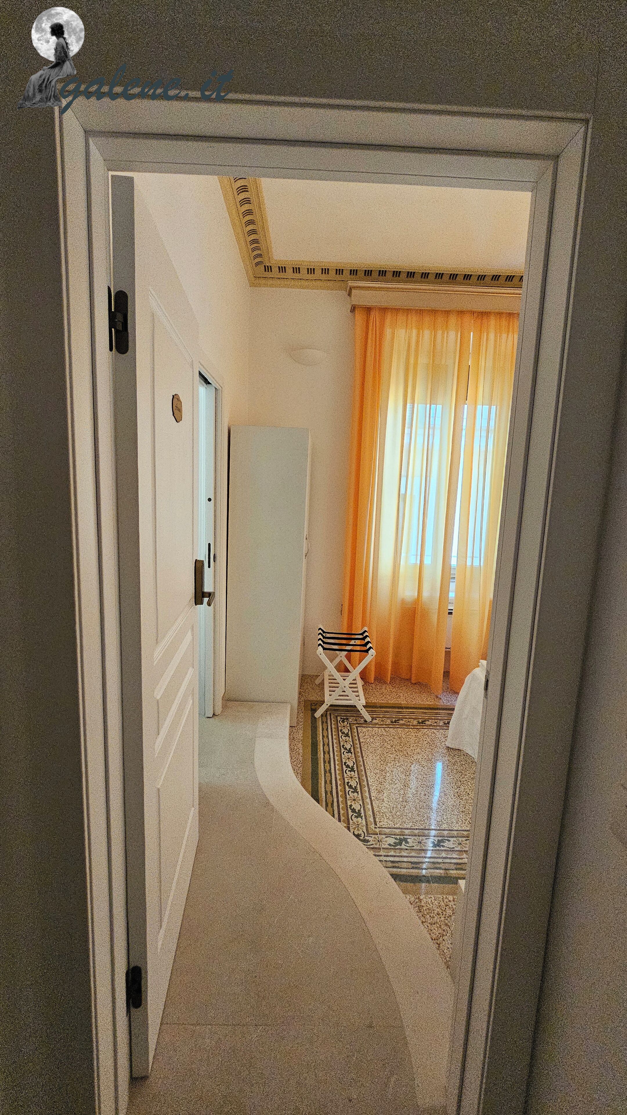 A hallway with a door leading to a room with a patterned rug, a small table, and a chair.