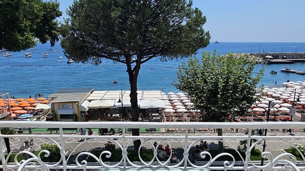 A seaside terrace with white metal chairs and a table, overlooking a beach with umbrellas and boats. - Galene - Beachfront in Costa d'Amalfi (Maiori)