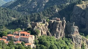 A historic town with a castle perched on a rocky cliff, surrounded by lush greenery and a valley.