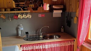 A kitchen with a sink, a stove, and a refrigerator. There is a sign that says "Eau Non Potable" and a window with a checkered curtain.