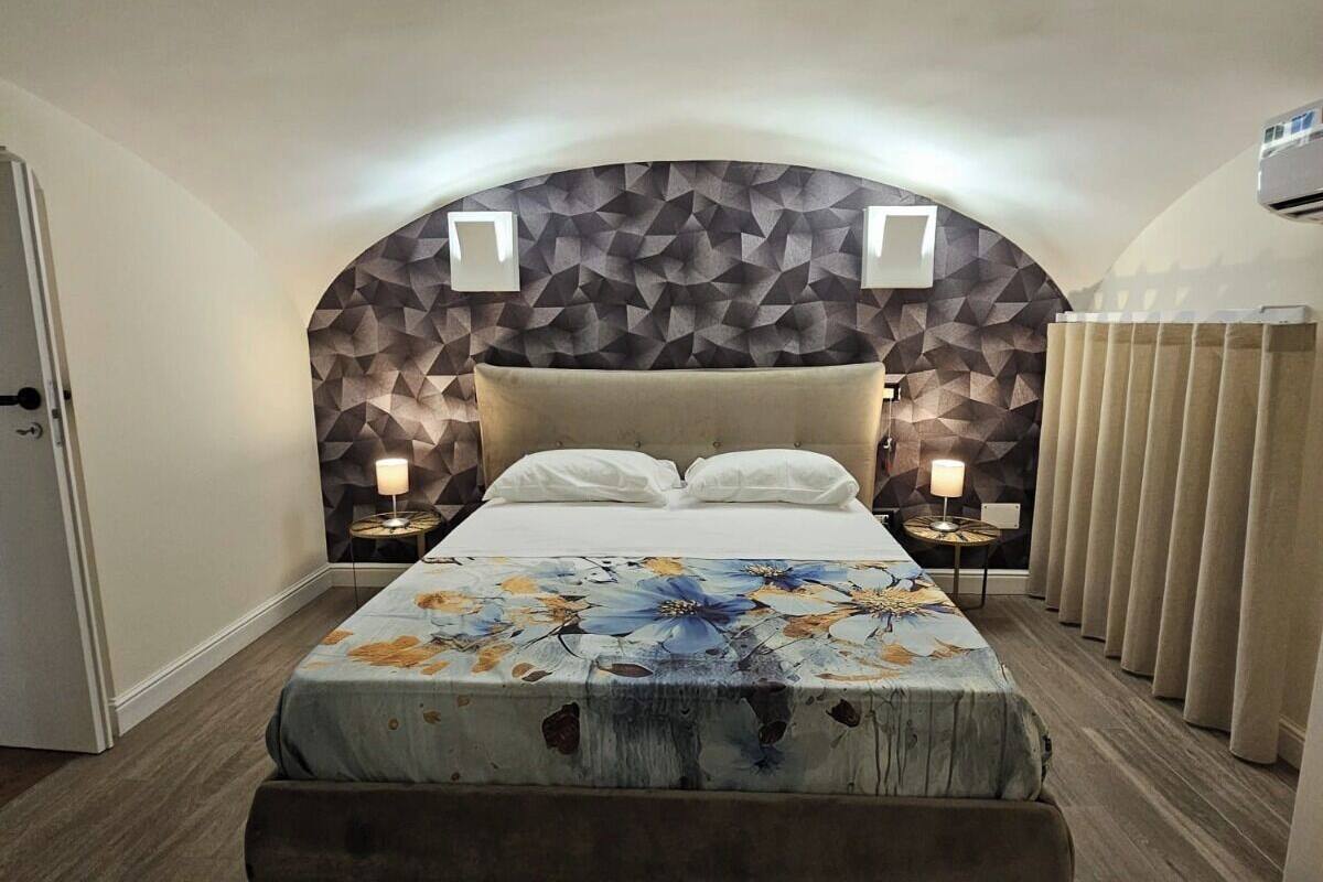 A bedroom with a large bed, a geometric-patterned headboard, two bedside lamps, and a window with curtains.