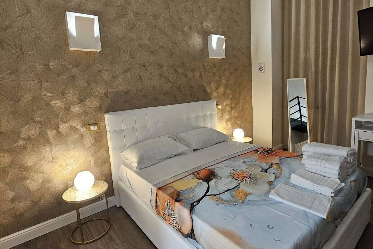 A bedroom with a large bed, two bedside lamps, a mirror, and a TV on a stand.