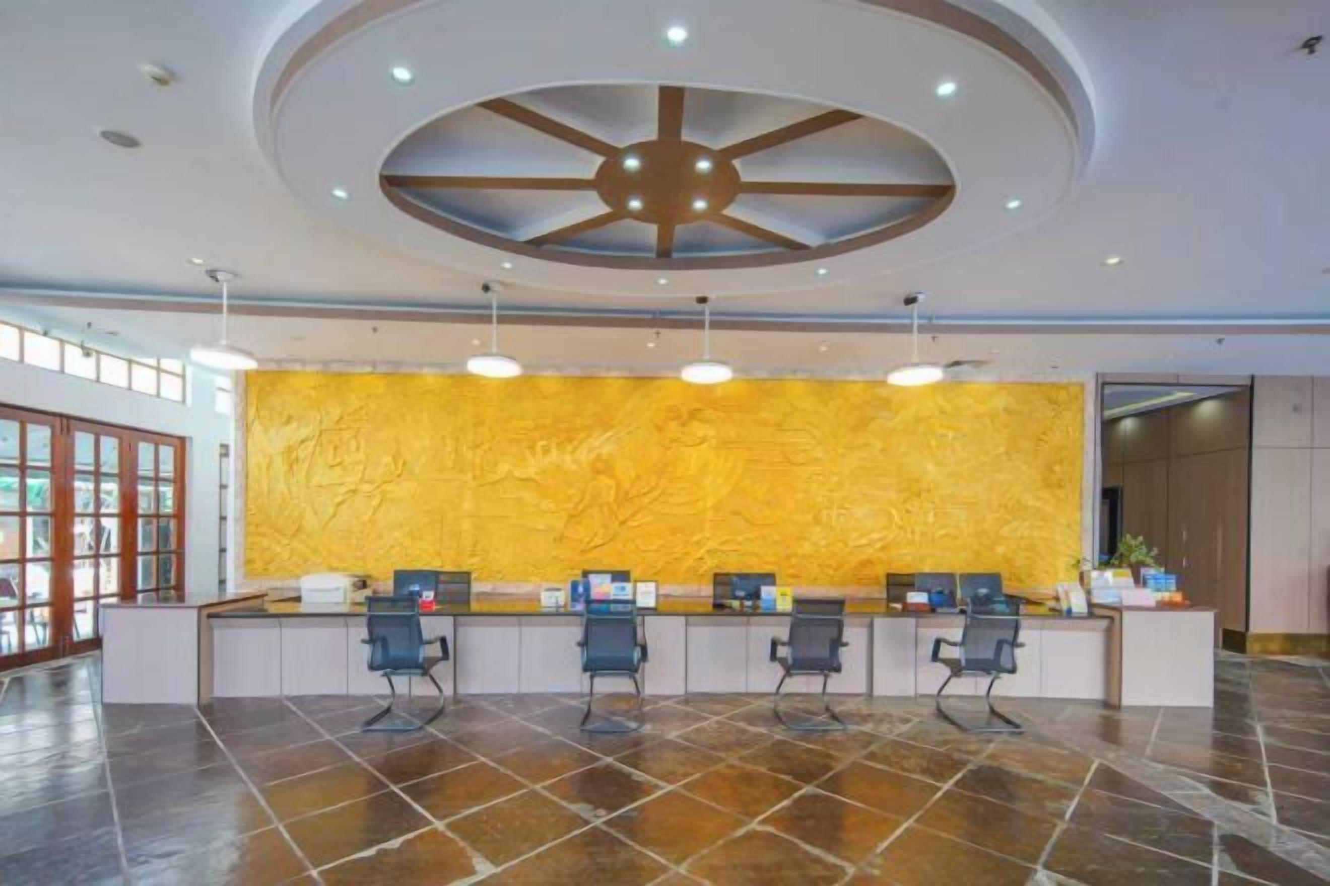 A reception area with a modern design, featuring a central desk with three chairs, a yellow textured wall, and a ceiling with a circular light fixture.