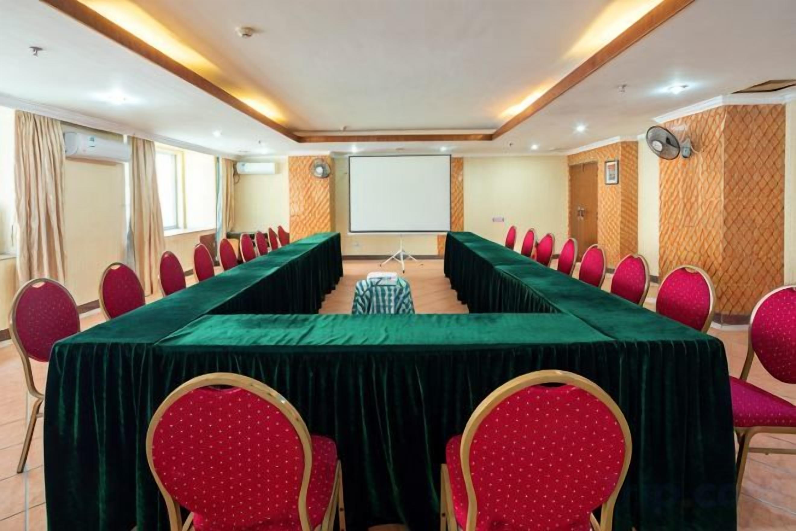 Una sala de conferències amb una taula llarga, cadires vermelles i una pantalla de projector.