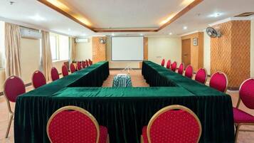 Una sala de conferències amb una taula llarga, cadires vermelles i una pantalla de projector.