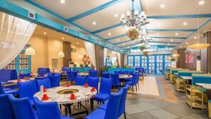 A spacious restaurant with blue chairs and tables, a chandelier, and a large window in the background. - Xinxing Garden Hotel (Sanyawan) (Sanya)