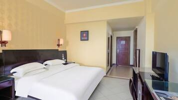 A hotel room with a large bed, bedside lamps, a television, and a desk with a computer.