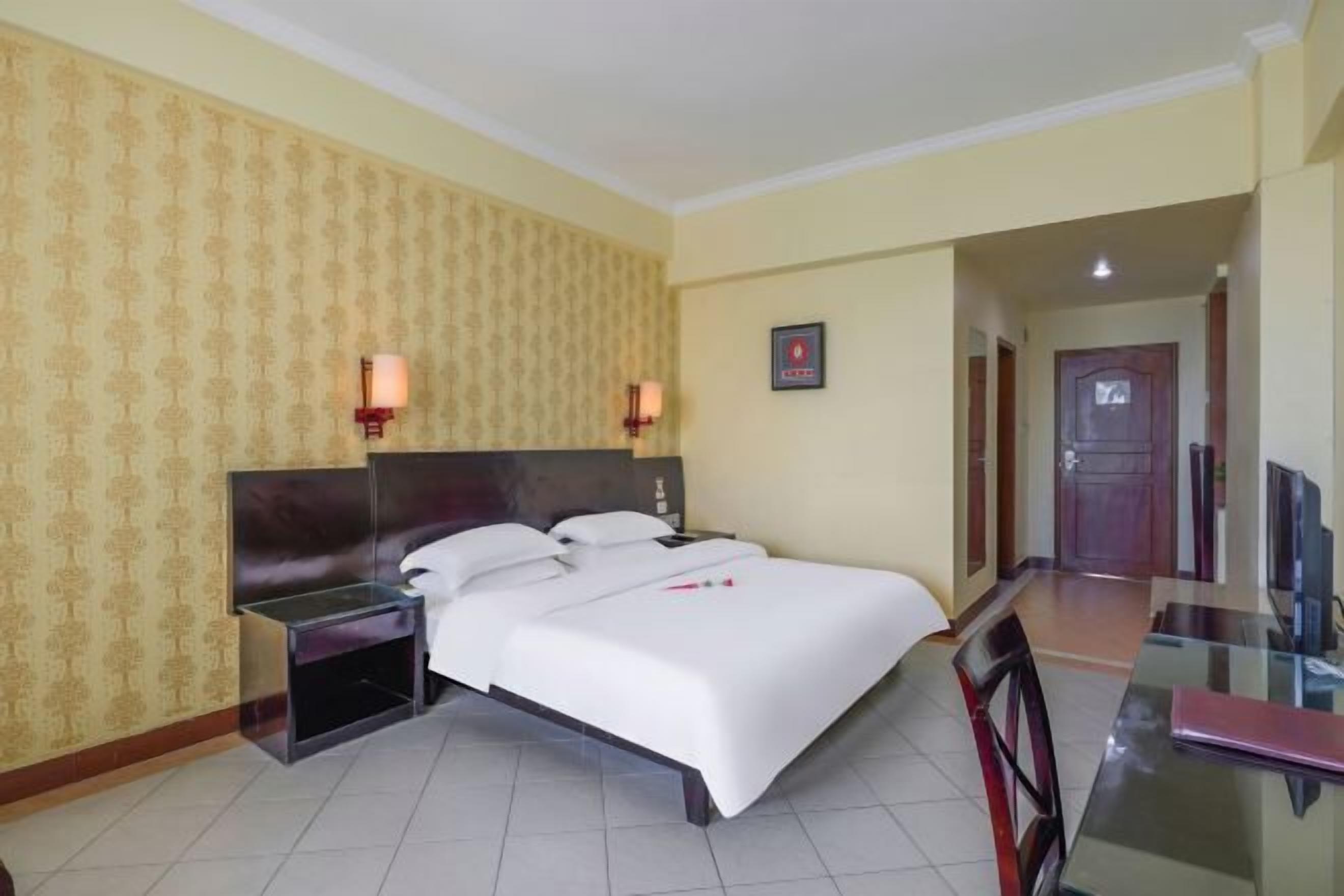 A hotel room with a bed, bedside tables, a desk, and a chair.