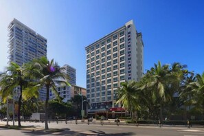 A high-rise building with multiple floors, surrounded by palm trees and a clear blue sky. - Xinxing Garden Hotel (Sanyawan) (Sanya)