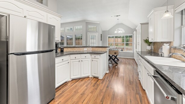 A spacious kitchen with white cabinetry, a stainless steel refrigerator, and a wooden floor. - Extraordinary Pool Villa - Outdoor Fun, Near Stadiums (North Richland Hills)