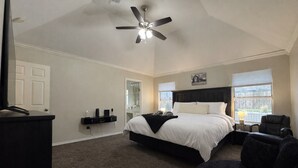 A bedroom with a large bed, a ceiling fan, a desk with a chair, and a window with blinds. - Extraordinary Pool Villa - Outdoor Fun, Near Stadiums (North Richland Hills)