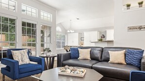A modern living room with a dark leather sofa, blue armchair, and a coffee table. - Extraordinary Pool Villa - Outdoor Fun, Near Stadiums (North Richland Hills)