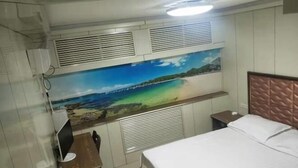 Een slaapkamer met een bed, een bureau met een computer, een wandairco en een grote strandmuurillustratie.