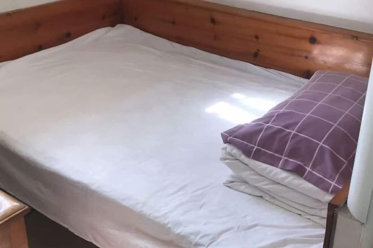 A single bed with a wooden headboard and a white mattress.