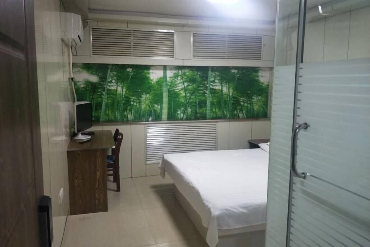 A bedroom with a bed, a desk, a chair, and a window with a forest view.