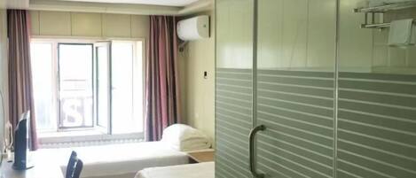 Habitación de hotel con cama, escritorio, silla, ventana con cortinas y una pared divisoria de vidrio.