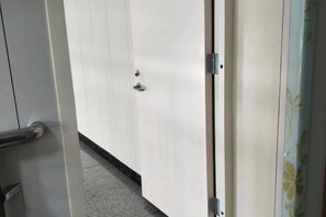 Une porte dotée d’une poignée métallique et d’un trou de serrure, qui donne sur une pièce dont le sol est recouvert de carreaux.