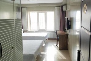 A hotel room with two beds, a desk, a television, and a window with curtains.
