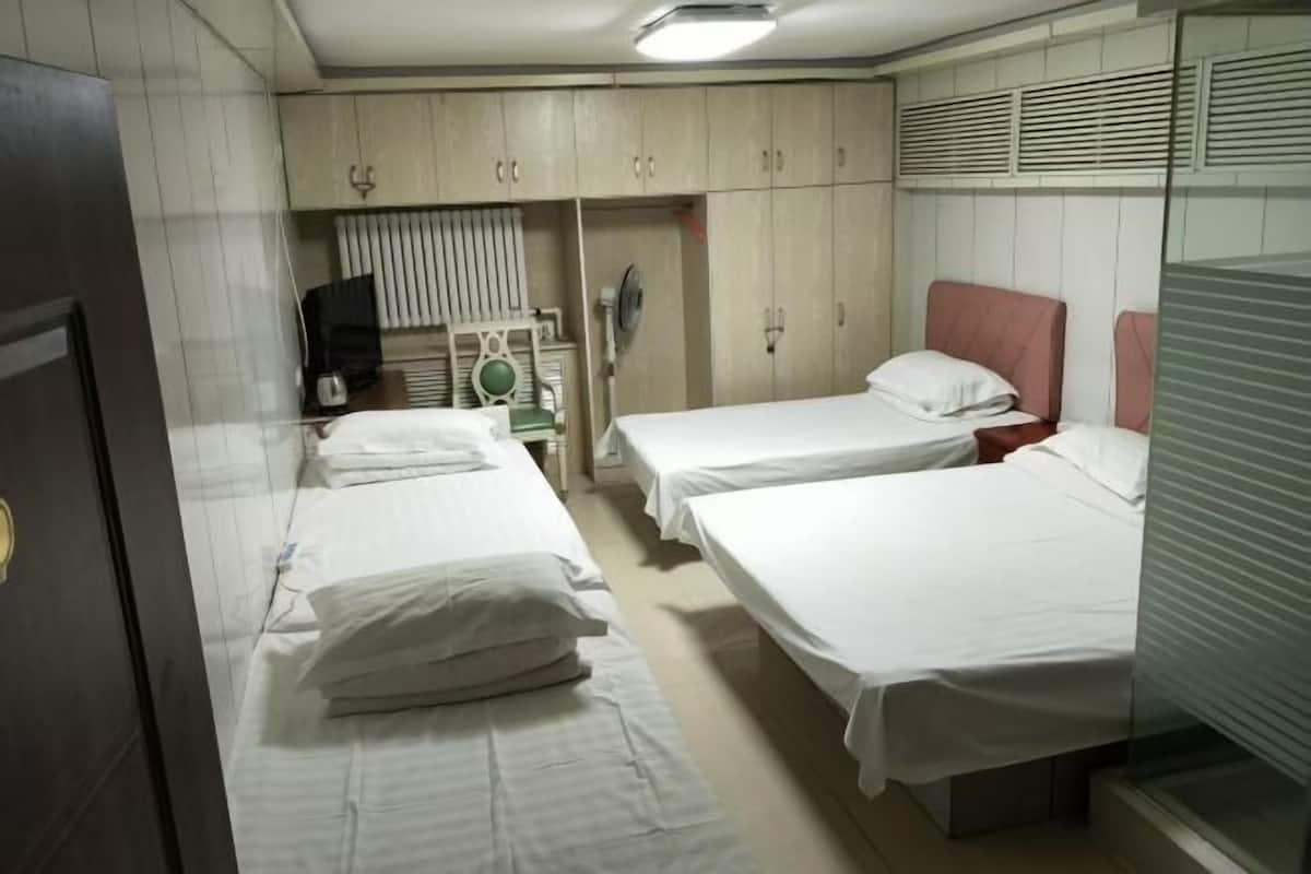 A hotel room with two single beds, a wardrobe, a television, and a fan.