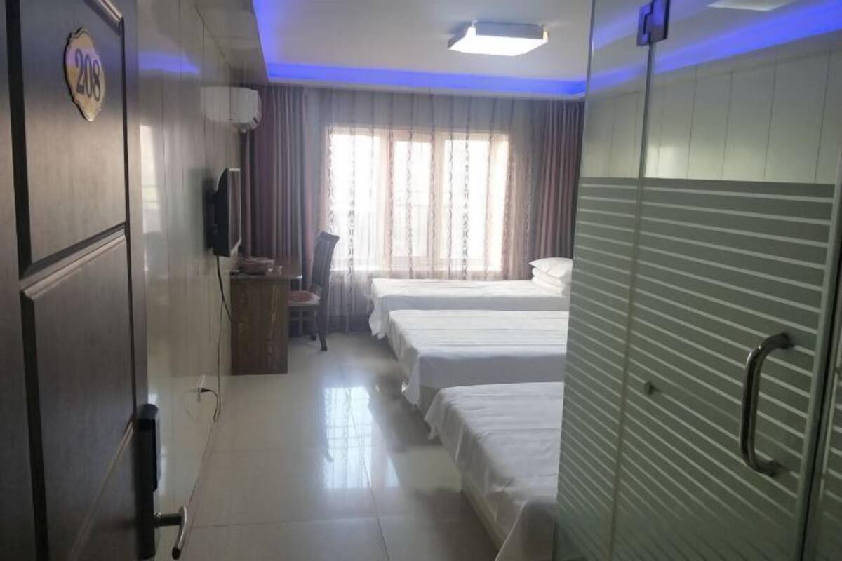 A hotel room with two beds, a television, a desk, and a window with curtains.