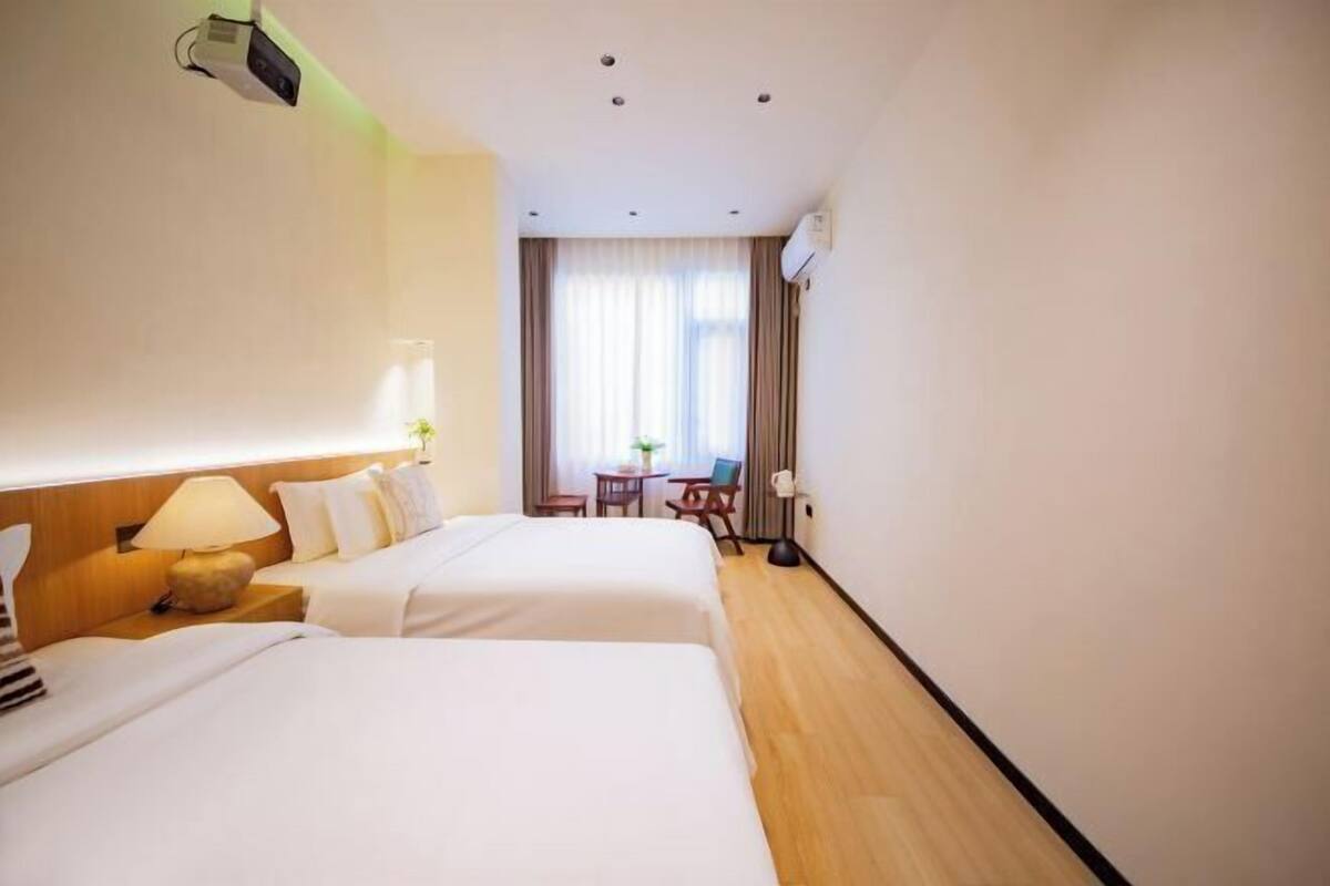 Hotelkamer met twee bedden, een bureau, een stoel, een raam met gordijnen en een projector aan het plafond.