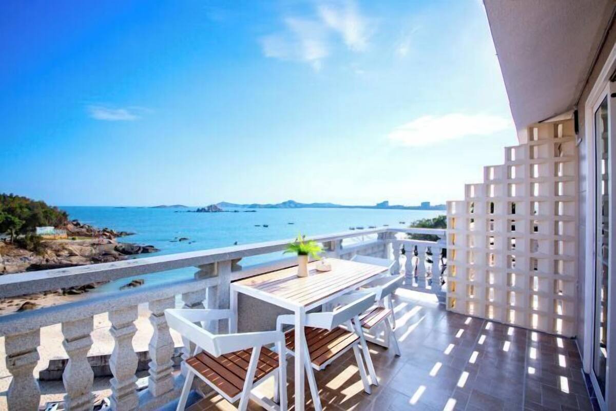 Een balkon met uitzicht op zee, witte meubels en een witte balustrade.