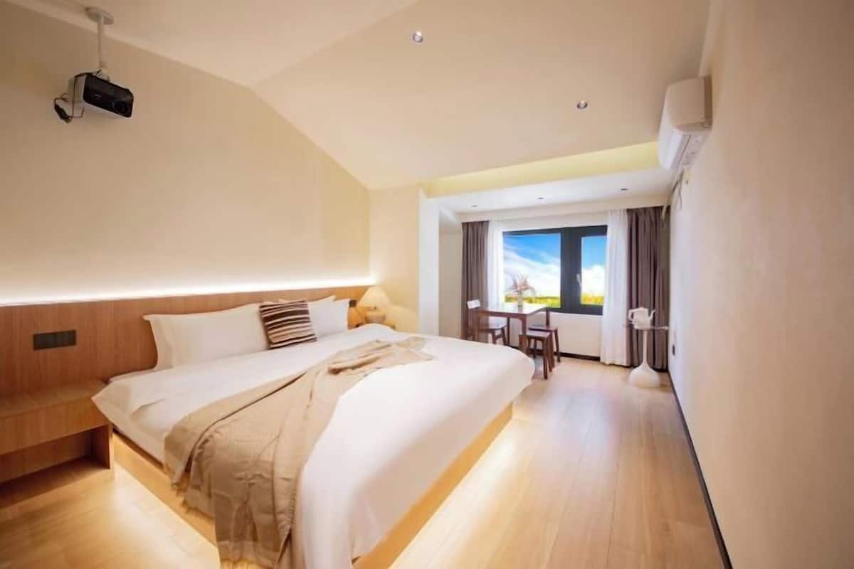 A hotel room with a large bed, a desk, and a view of the outdoors.