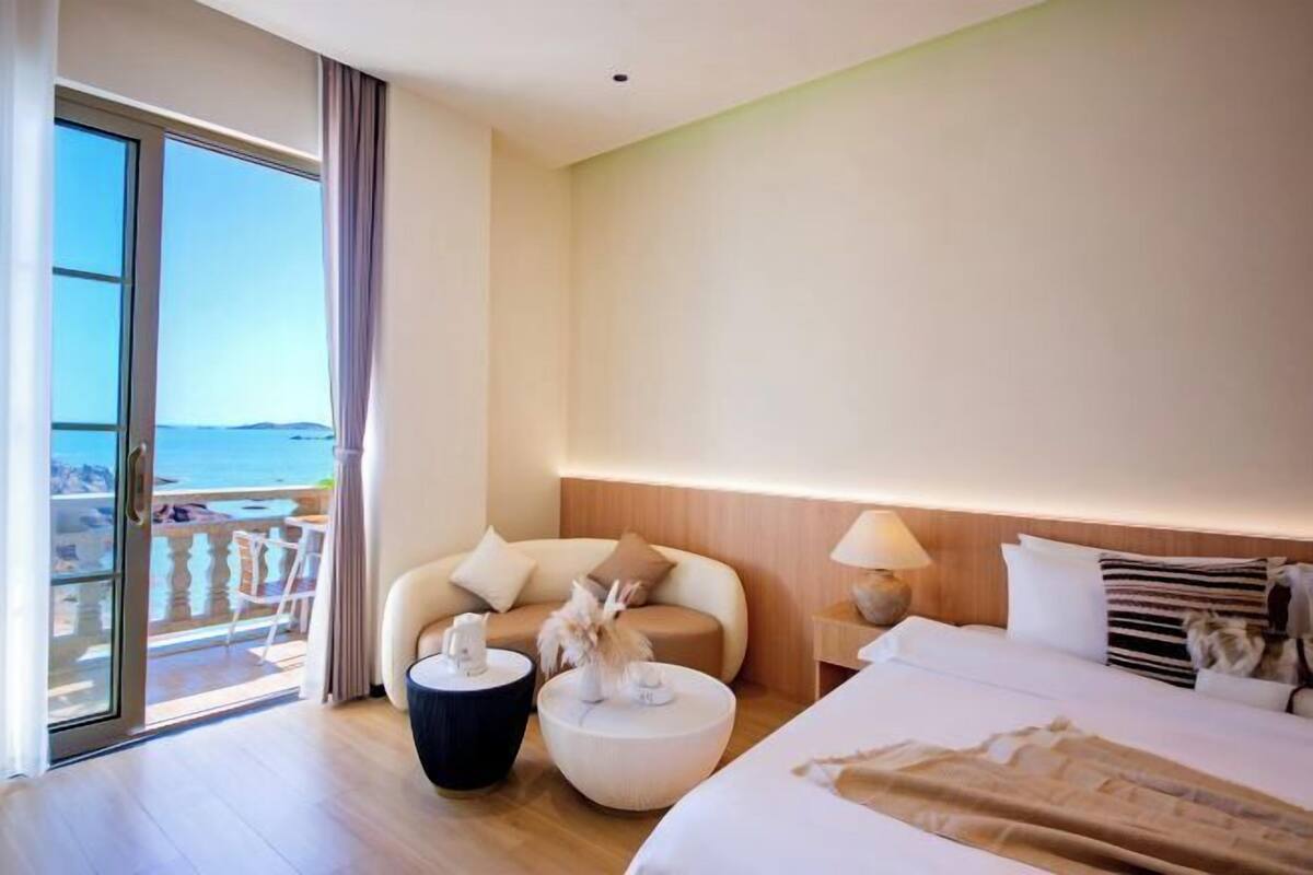 Een hotelkamer met balkon, een bed, een slaapbank, een klein rond tafeltje en een nachtkastje met lamp.