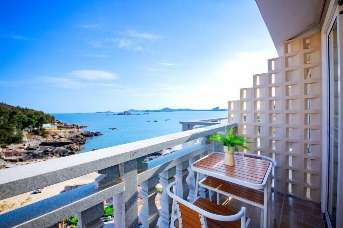 Een balkon met uitzicht op zee, een houten tafel en een bloempot.