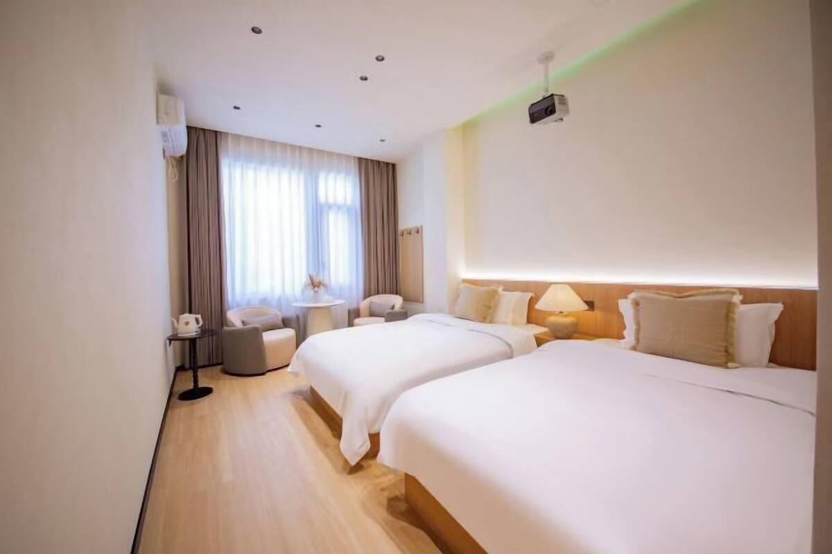 Hotelkamer met twee bedden, een bureau, een stoel, een lamp en een raam met gordijnen.
