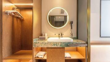 A modern bathroom with a wooden vanity, a round mirror with a light, a sink, and a towel rack.