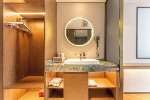 Un baño moderno con tocador de madera, un espejo redondo con luz, un lavamanos y un perchero para toallas.