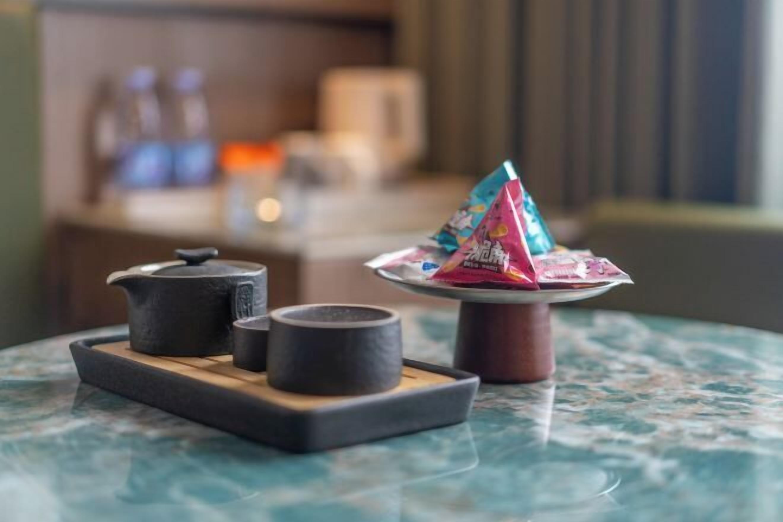 A table with a teapot, cups, and a packet of snacks.